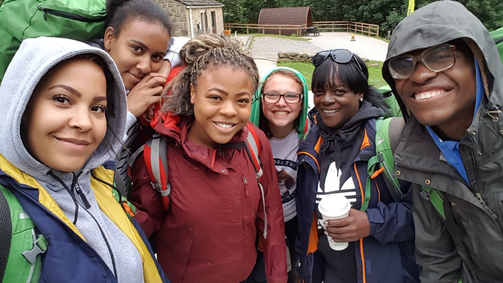Six smiling young people taking part in the Duke of Edinburgh Awards Scheme. They are outside, wearing wet weather clothing and carrying rucksacks.