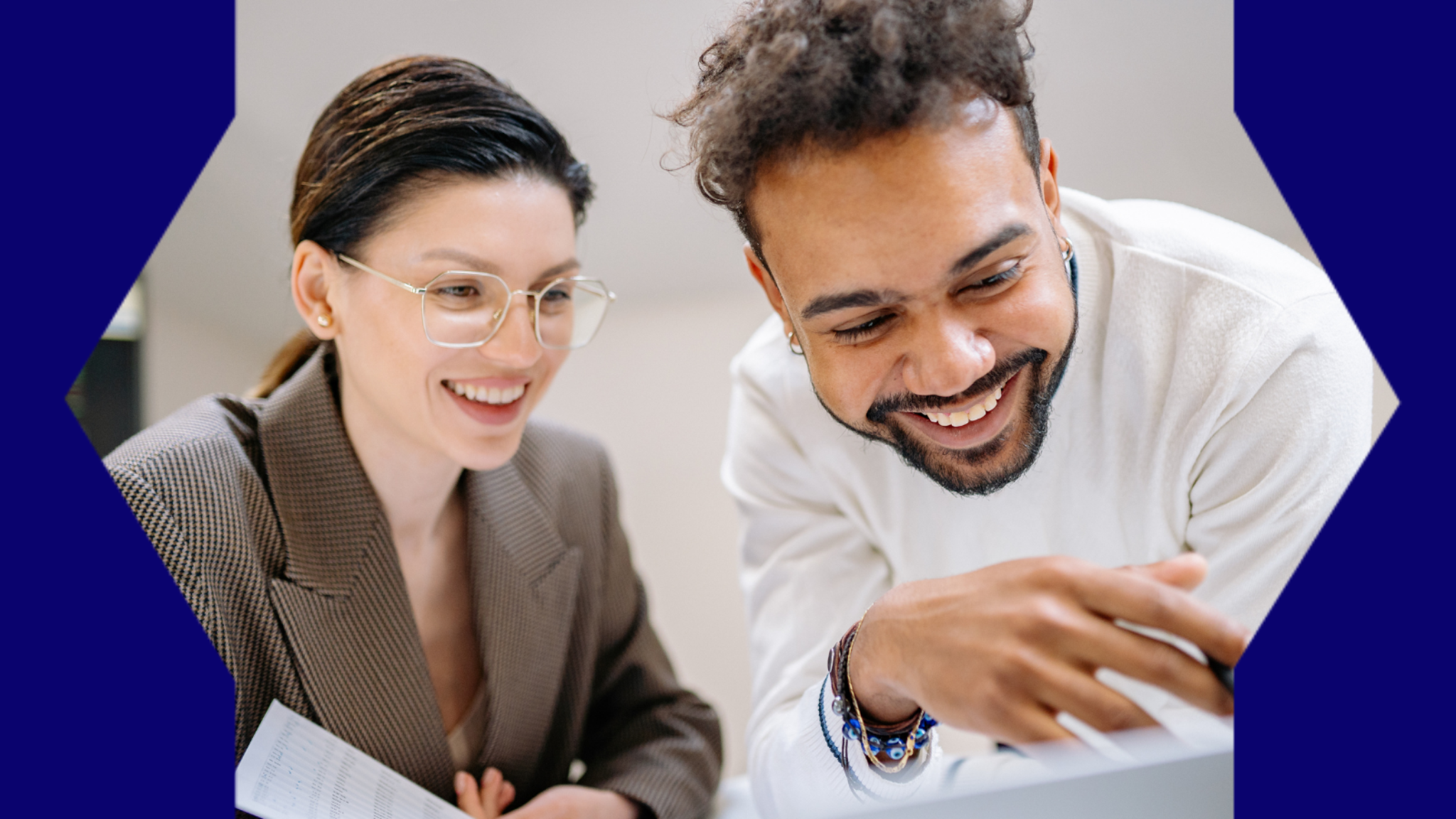 Two colleagues smiling as they discuss work over a laptop computer.