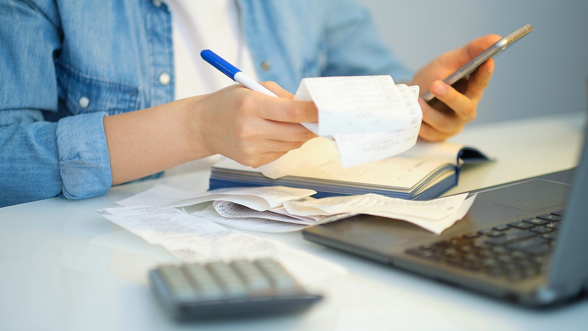 A person sits at a desk with a laptop, looking through receipts.