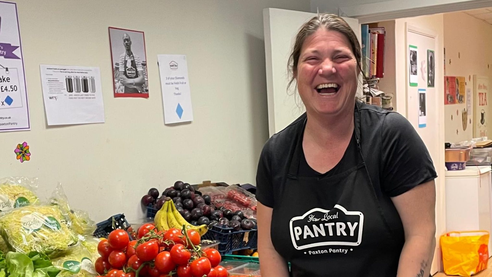 Volunteer Emma stands in front of a shelf of fresh produce at Paxton Pantry