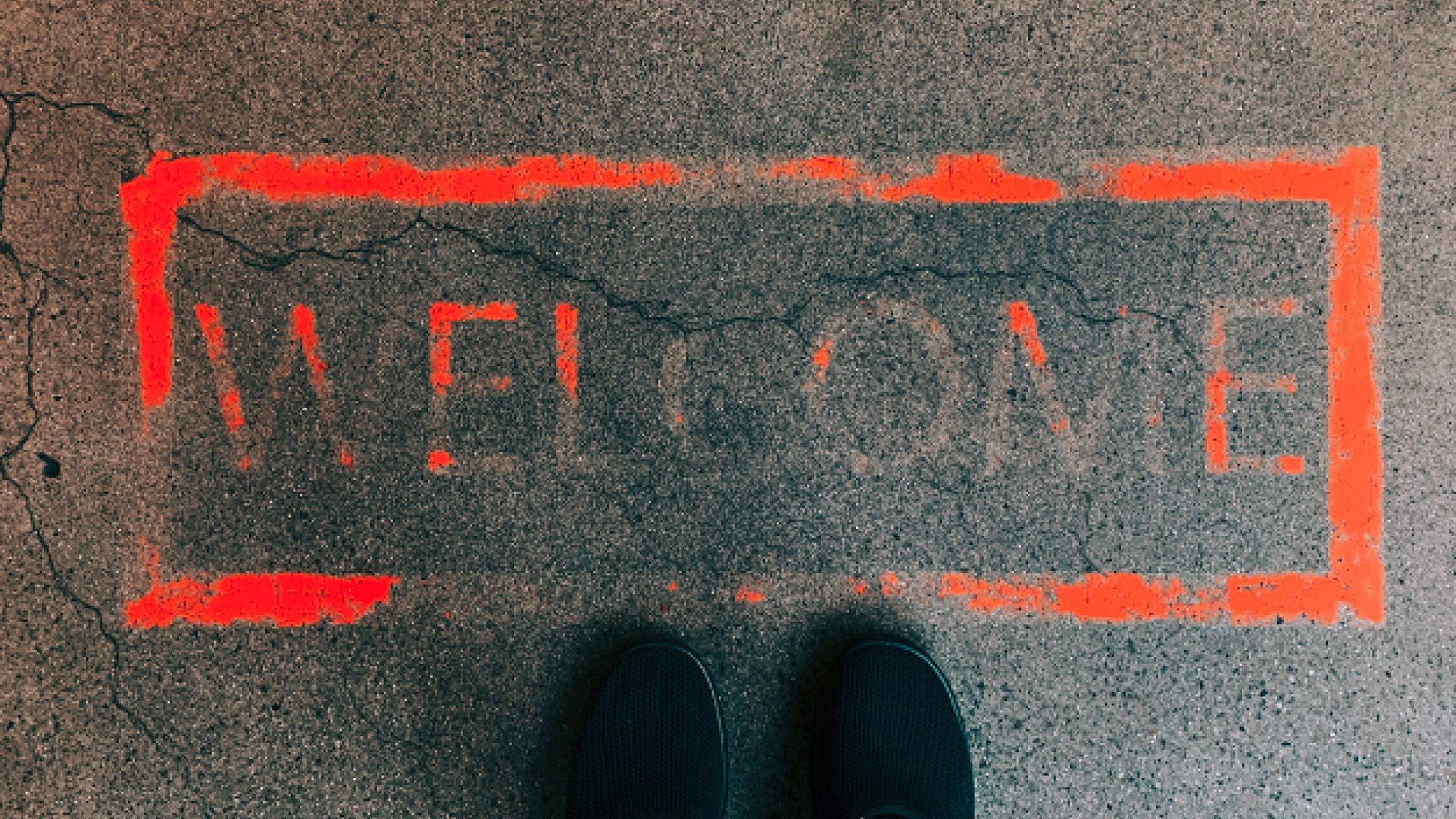 Welcome painted on the floor with red paint and a pair of black shoes standing next to the sign