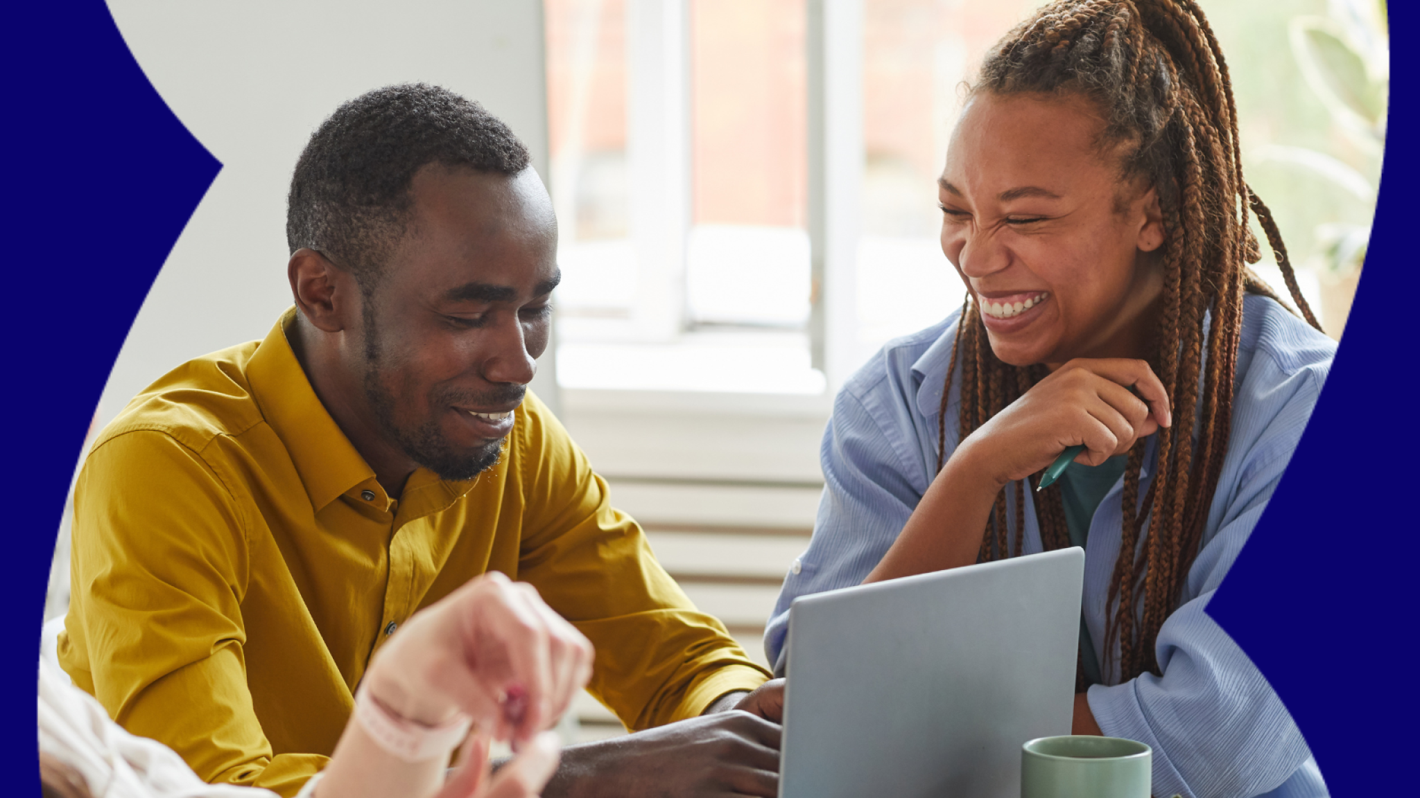 Two colleagues smiling as they work on a laptop.