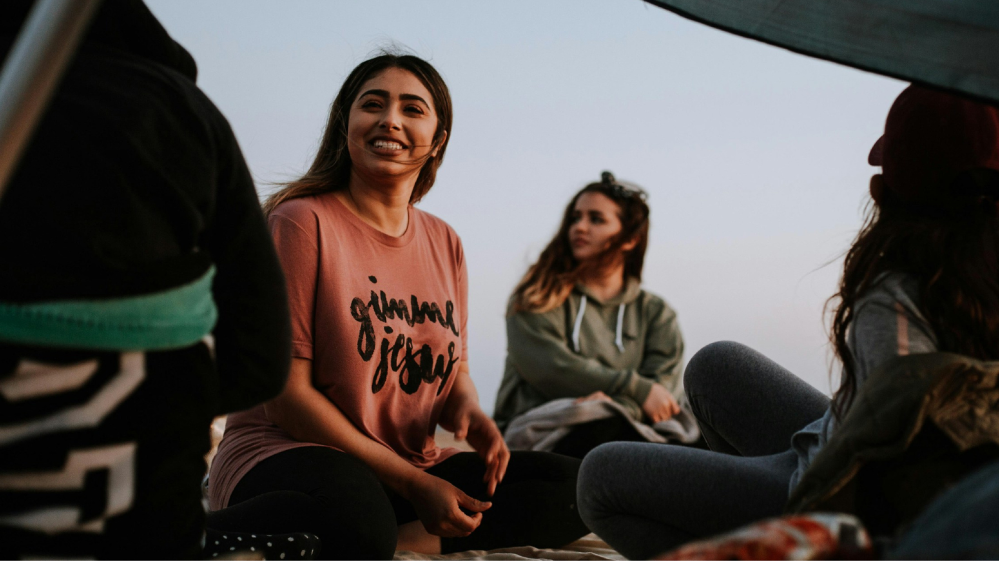 Three young women sitting outside, looking relaxed and wearing casual clothing